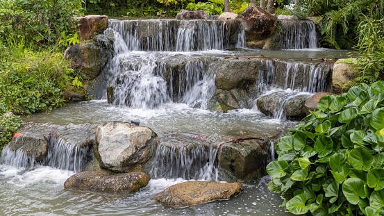 A small waterfall cascading over large rocks in a garden setting with a powerful, rushing current