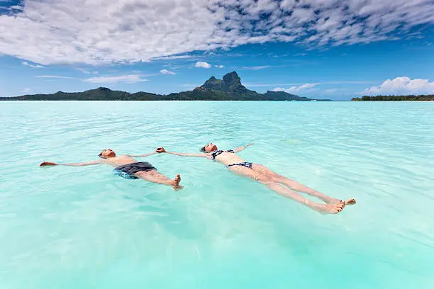 Mother and Son in Summer Vacation. Woman relaxing together with her young son in the turquoise waters of Bora Bora Lagoon. Swimming together on the back, holding hands, enjoying the sun. Famous Bora Bora Mount Otemanu on the horizon. Bora Bora Island, Society Islands, French Polynesia.