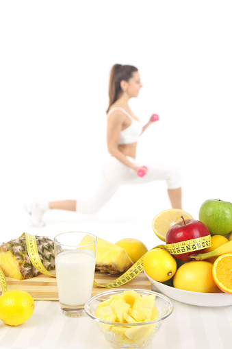 Healthy food and drink in front of fit young woman exercising with dumbbells-isolated on white background