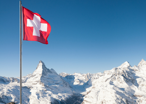 The white cross on red background of the Swiss national flag flying high above the Alps, with the Matterhorn directly underneath the flag.  Taken at the ski resort of Zermatt.