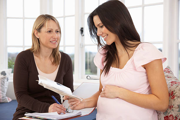 Pregnant Woman Reading Information Booklet At Home With Health Visitor Pregnant Woman Reading Information Booklet At Home Chatting With Health Visitor midwife photos stock pictures, royalty-free photos & images