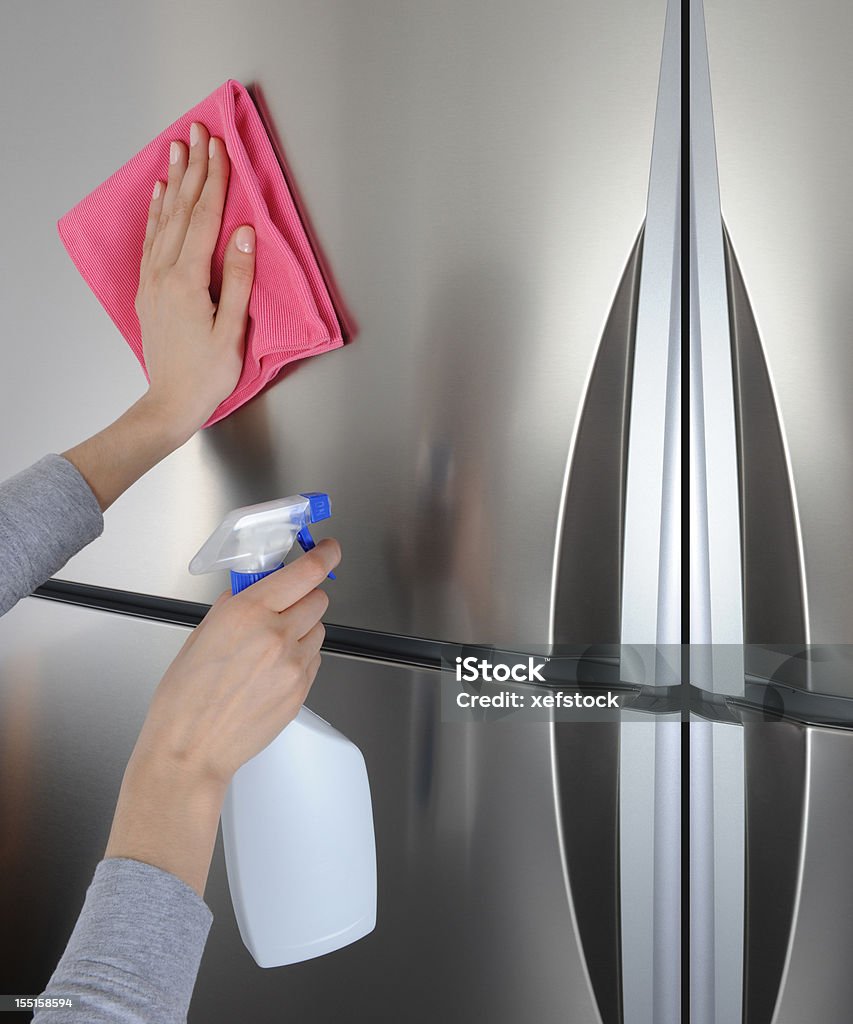 Cleaning surface of refrigerator The woman cleaning surface of inox refrigerator with pink rag and spray.  Cleaning Stock Photo