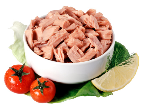 A bowl with canned pink tuna chunks on a lettuce leaf with tomato cherries,lemon and anise,isolated on white,clipping path included.