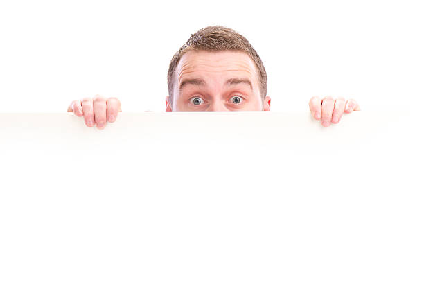 istock surprised young male peeking over sign 155159983