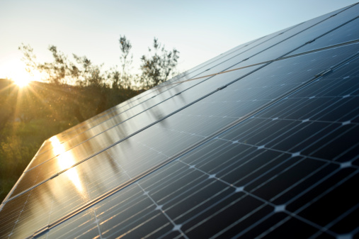 Close up of photovoltaic solar panels with warm sun light bursting above horizon.