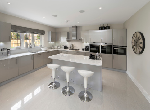 a spacious kitchen in a luxury new house prepared by an interior designer. Three kitchen stools sit in front of a large island. All cupboard fronts are silver grey.