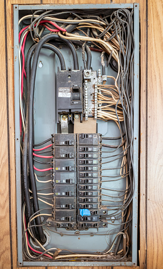 Wires running to and from an electrical panel with different sized circuit breakers and fuses plus missing, damaged and dirty parts.