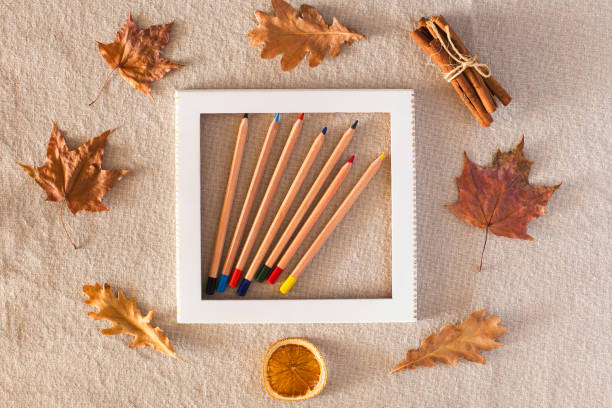 Autumn composition with a frame with colored pencils in the center, around autumn dry leaves, dried orange, cinnamon on a background of linen fabric. Flat lay, copy space, fall concept.