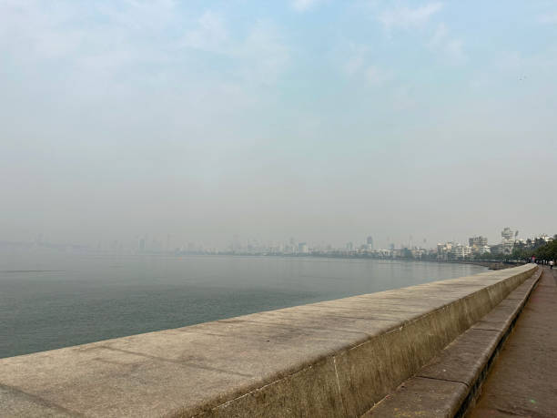 Stock photo showing close-up view of a manmade, sea defence of a concrete, seawall, which has been constructed to prevent flooding of the promenade of Marine Drive, Mumbai, India during high tide. imagen de la pared marina marine drive, mumbai, india, hormigón, defensa del malecón, gestión costera, prevención de la erosión, agua de mar, paseo en forma de c, edificios art deco y rascacielos que bordean la playa pública de girgaon chowpatty.