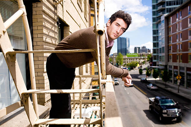An attractive man leaning over a fire escape over looking the city on a summer day.