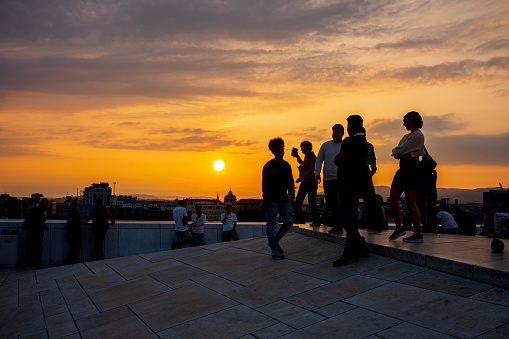 Oslo, Norway, June 20, 2023: Tourists view a sunset from the Oslo Opera House, which was built in 2008 with the intention to allow visitors to walk up its marble-covered roof.