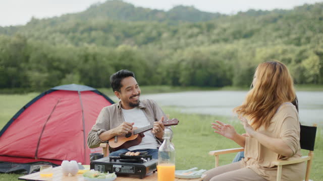 Happy family singing, dancing and play Ukulele at camping tent on summer weekend vacation.