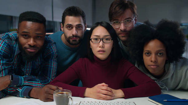 Surprised diverse business people looking at computer screen in dark office. Multiethnic colleagues look at camera together