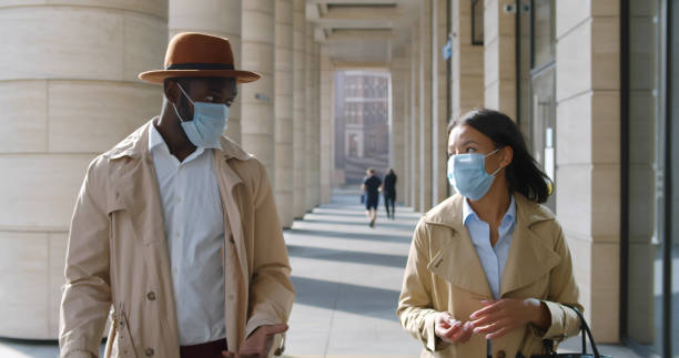 istock Young colleagues in medical mask walking outside modern building 1551846537