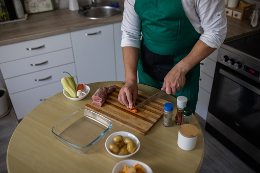 Hands holding fork and knife and ready to eat raw pork meat on the wooden cutting board on dark background. Nonvegetarian concept, copy space.