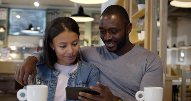 istock Happy mixed race couple using mobile phone while drinking coffee in cafe 1551869840