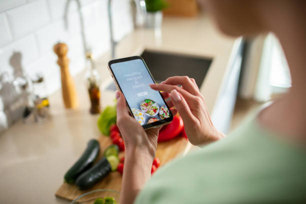 istock Young woman using a diet app on her phone while preparing a healthy food dish at home 1551879771