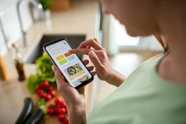 istock Young woman using a diet app on her phone while preparing a healthy food dish at home 1551883364