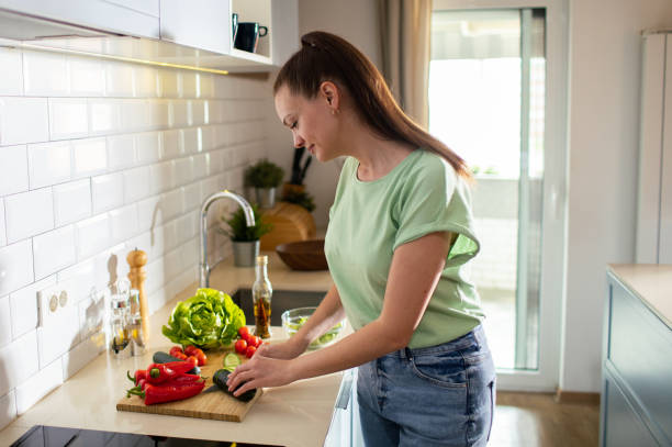 istock Young woman cutting and preparing vegetables in a kitchen at home 1551884411