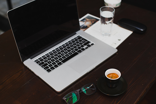 Modern work place, laptop, cup of fresh coffee, glass of water and glasses on wooden table