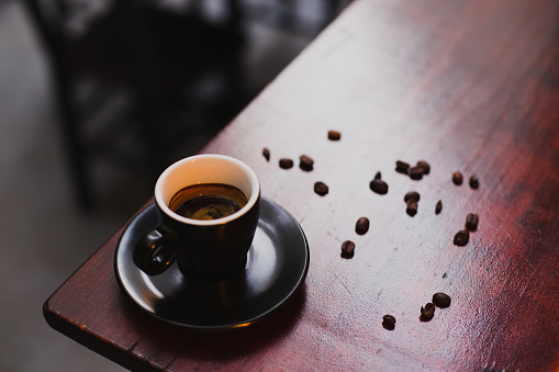 Cup of fresh coffee with coffe beans around it on old wooden table