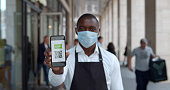 Medium shot of african male in apron and safety mask show online vaccine certificate on camera