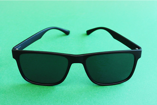 Fashion summer concept. Copy space. Black trendy generic sunglasses on a green paper background.