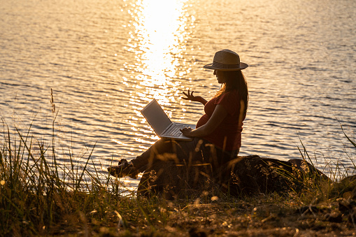 Las personas y la naturaleza. Freelancer embarazada trabajando en una computadora portátil en la orilla del lago. photo