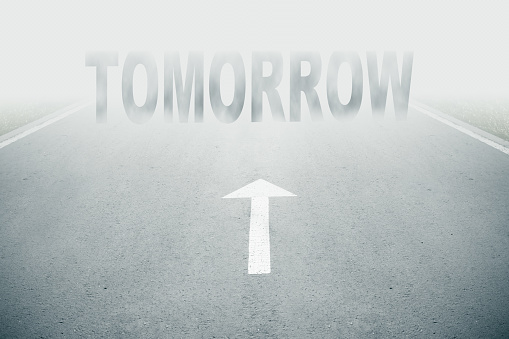 Tomorror text on asphalt road with white arrow sign on road goes into fog. Direction way sign. Moving forward in uncertainty tomorrow concept. Unclear tomorror ahead or negative tomorrow concept