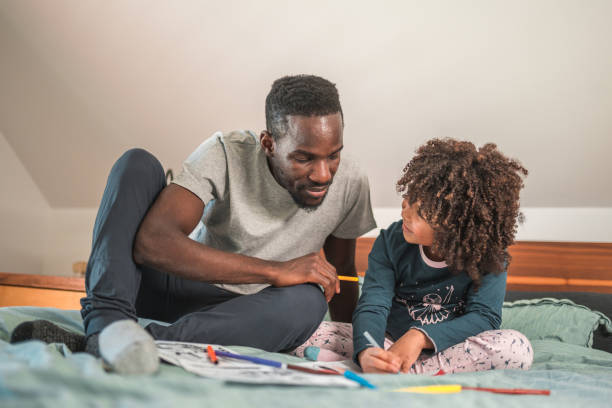 istock Handsome Black American Man and his Cute Son Coloring Together on the Bed 1551948614
