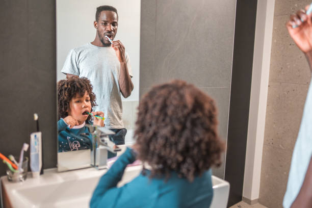istock Cute African-American Boy Learning to Brush Teeth With Dad 1551948619