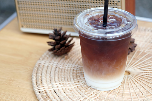 An iced coffee in a plastic cup sits on a wooden table, surrounded by natural decorations