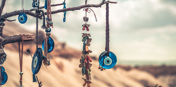 Amulets against evil eye hanging on tree in front of sandy mountain in Cappadocia, Turkey