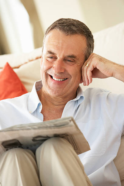 istock Senior Man Relaxing On Sofa At Home Reading Newspaper 155217220