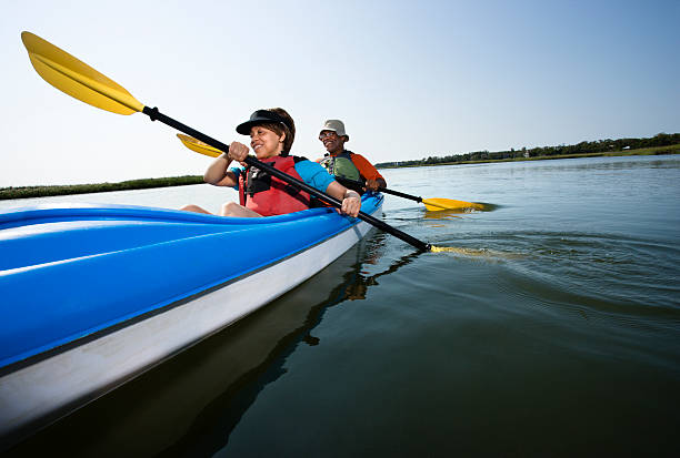 Couple kayaking. Low angle of African American middle-aged man and woman paddling kayak. bald head island stock pictures, royalty-free photos & images