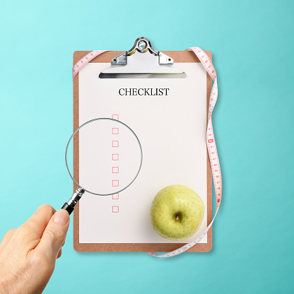 Close-up of looking through a checklist with a magnifying glass, on light blue background.
Blue apple on the checklist.
Dieting concept
