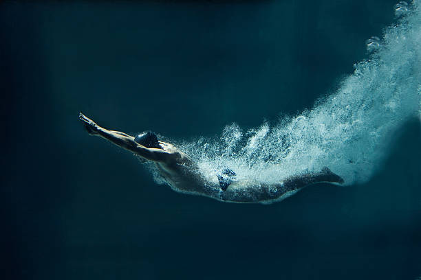 schwimmer unter wasser nach dem sprung auf blauem hintergrund - schwimmen stock-fotos und bilder