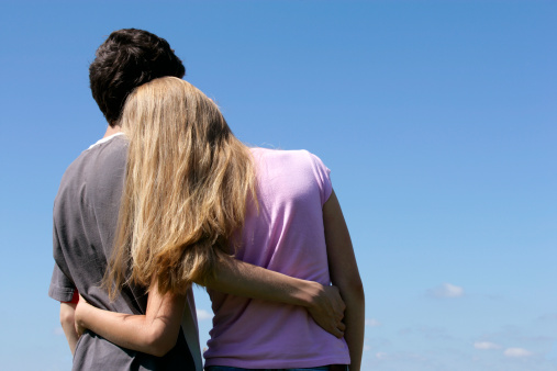 Romantic teenage couple looking at blue sky hugging