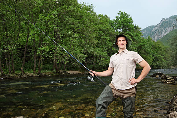 A young fisherman posing while fishing on a river with trees in the background
