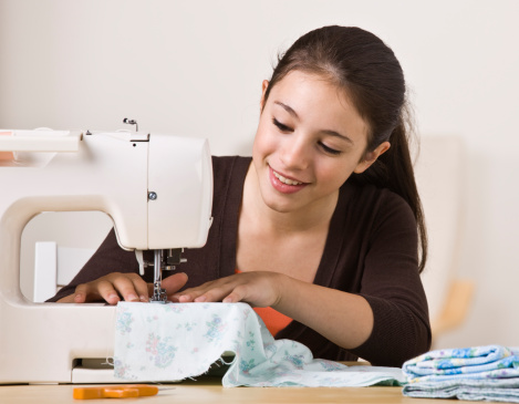 A beautiful, smiling young girl sewing on a sewing machine.  Horizontally framed shot.  