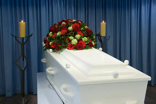 A white coffin in a mortuary with a flower arrangement
