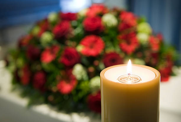 Burning candle next to bundle of flowers A burning candle with a white coffin and a flower arrangement on the background in a mortuary funeral parlor photos stock pictures, royalty-free photos & images