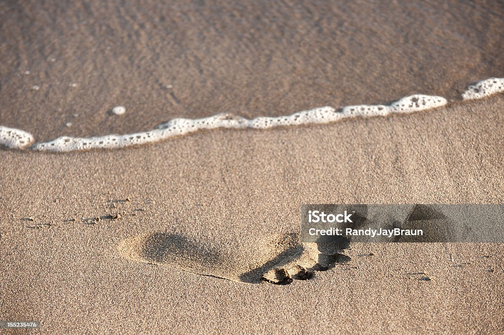 Wave Approaching Footprint in Sand The wash of an ocean wave is quickly approaching a single human footprint in the sand. Barefoot Stock Photo