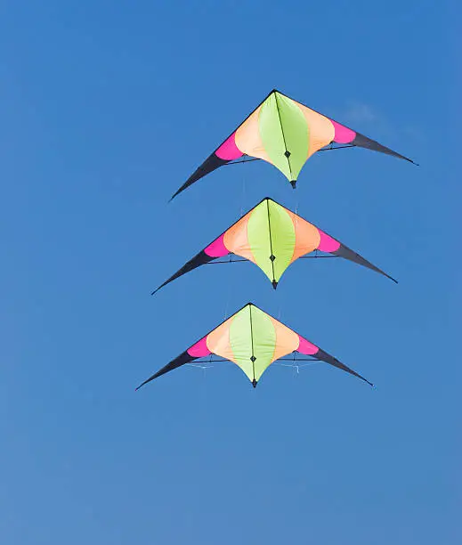 Three identical stunt kites on a blue sky background.
