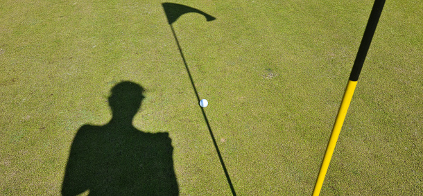 Shadow of golfer near flag on green green. Golf and ball hole