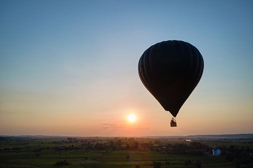 Aerial view of big hot air baloon flying over rural countryside at sunset.
