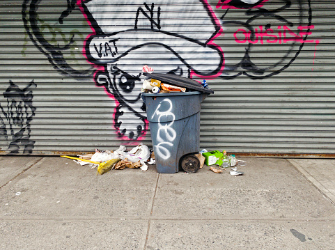 Bronx, New York - April 7, 2023: Trash can with garbage spilling on street in front of local business.