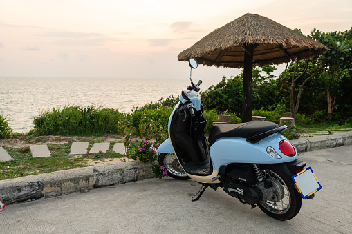 the blue moped is parked on the ocean shore against the background of a beautiful sunset in the yellow sky