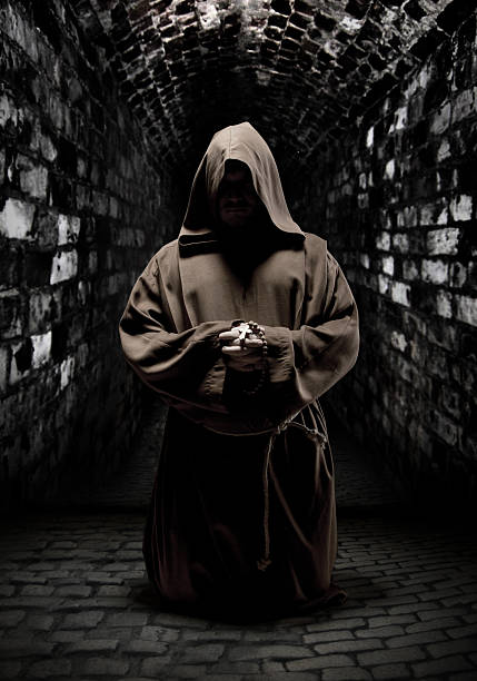 Praying monk in dark temple corridor Mystery monk praying on kneels in dark temple corridor ceremonial robe stock pictures, royalty-free photos & images