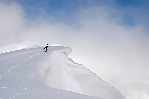 Extreme skier looking over a cornice to check the slope before start riding. The wind has shaped beautiful snow spine down the mountain.